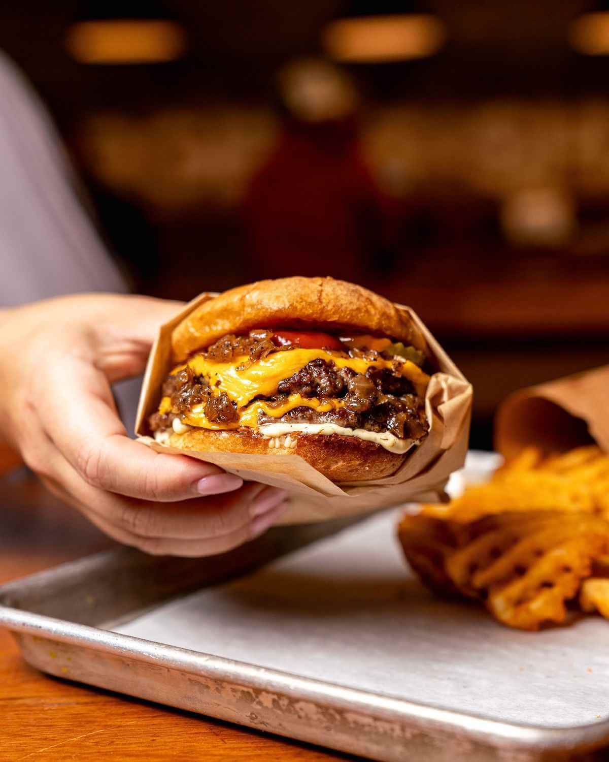 Гость Qazmaq держит бургер с салатом, сыром и соусом